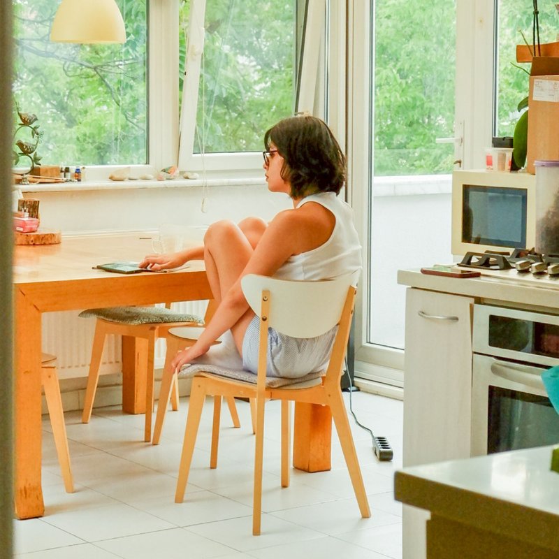 Eine Frau sitzt allein am Küchentisch und schaut aus dem Fenster in den Garten.