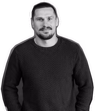 Man with short dark hair and beard wearing a textured dark sweater, smiling slightly.