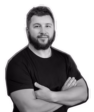 Man with beard and short hair wearing a black t-shirt with arms crossed, smiling slightly.