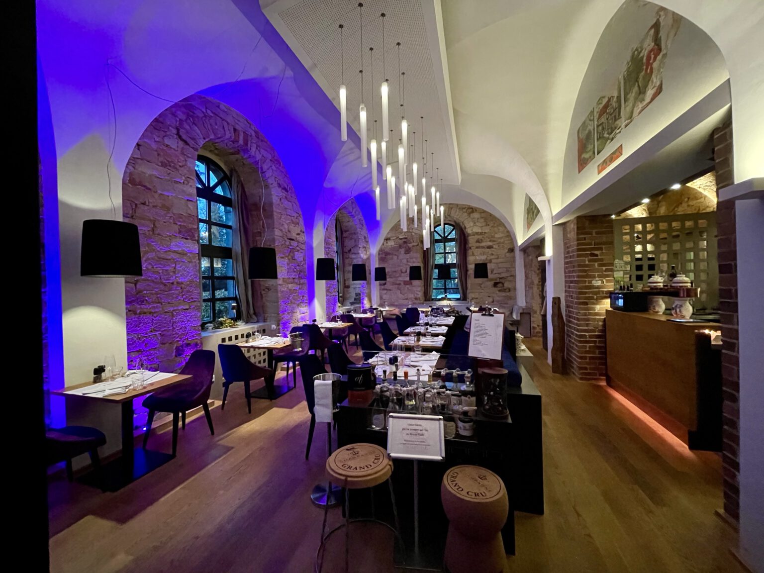 Gemütliches Restaurant mit blau beleuchteten Steinbögen, elegant gedeckten Tischen und modernen Hängeleuchten.