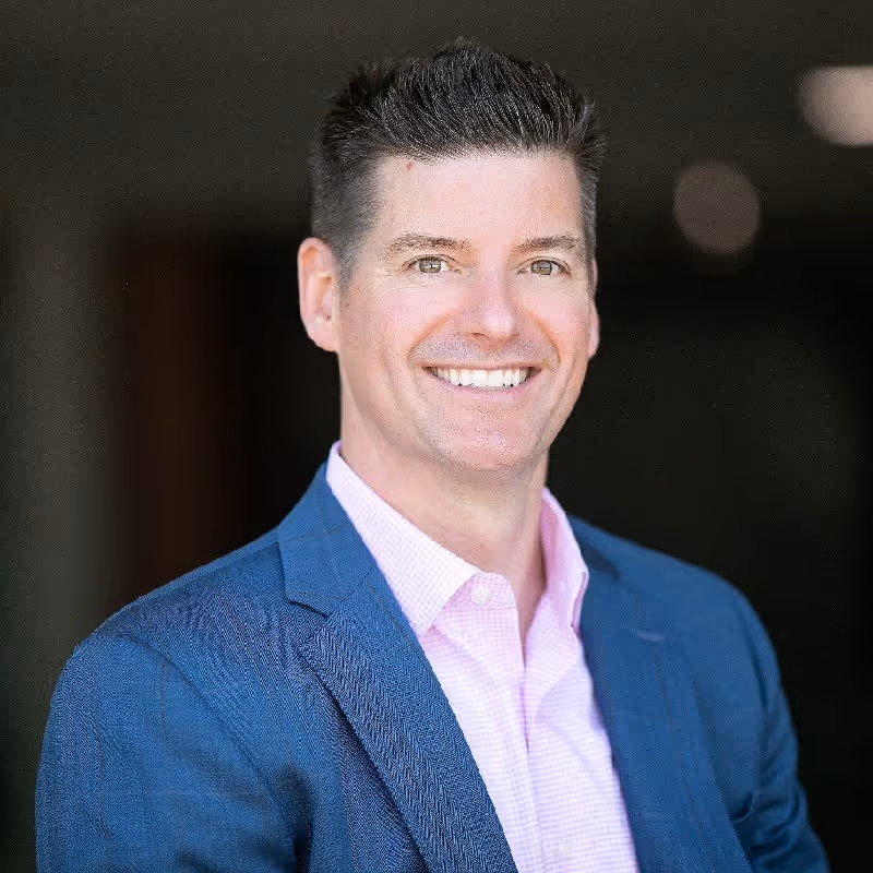 Chris Krackeler is a smiling businessman in a blue suit with a pink shirt