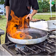 Chef cuisinier réalisant un flambage à la poêle lors d'un service traiteur gastronomique.