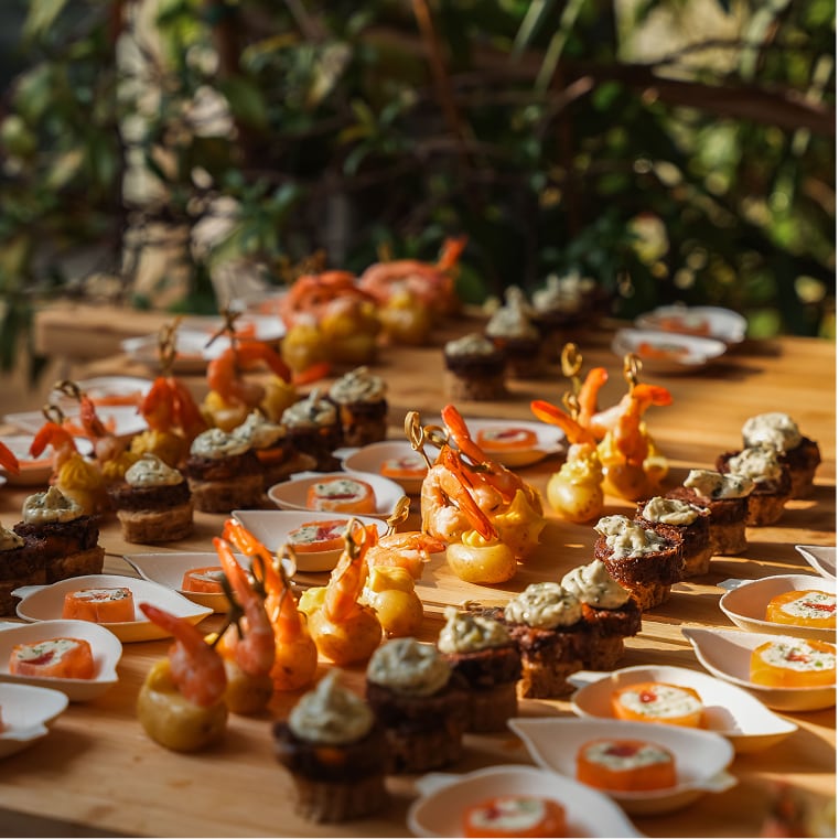 Planches de bouchées apéritives disposées sur une table en bois avec un assortiment de crevettes enrobées de pâte dorée, petites tartines garnies de mousse et tranches de saumon sur lit de sauce.