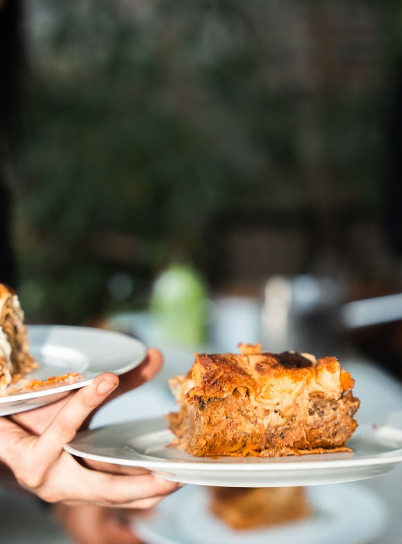 Une main tenant une assiette blanche avec une grande portion de lasagnes cuites, montrant les couches de viande et de fromage fondant.