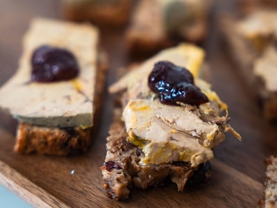 Toasts de pain aux noix garnis de foie gras et d'une cuillerée de chutney foncé sur une planche en bois.