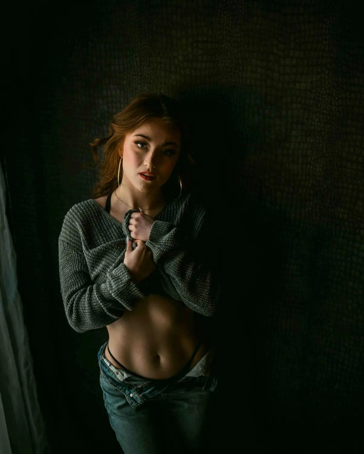 Sensual young woman, lifting sweater to expose stomach, jeans unbuttoned. 