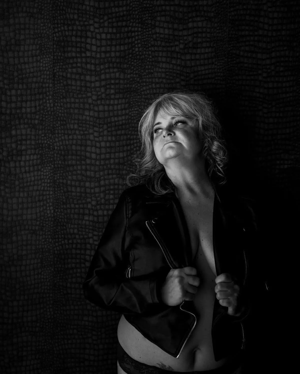 Beautiful, mature woman, topless in black leather jacket, looking off frame.