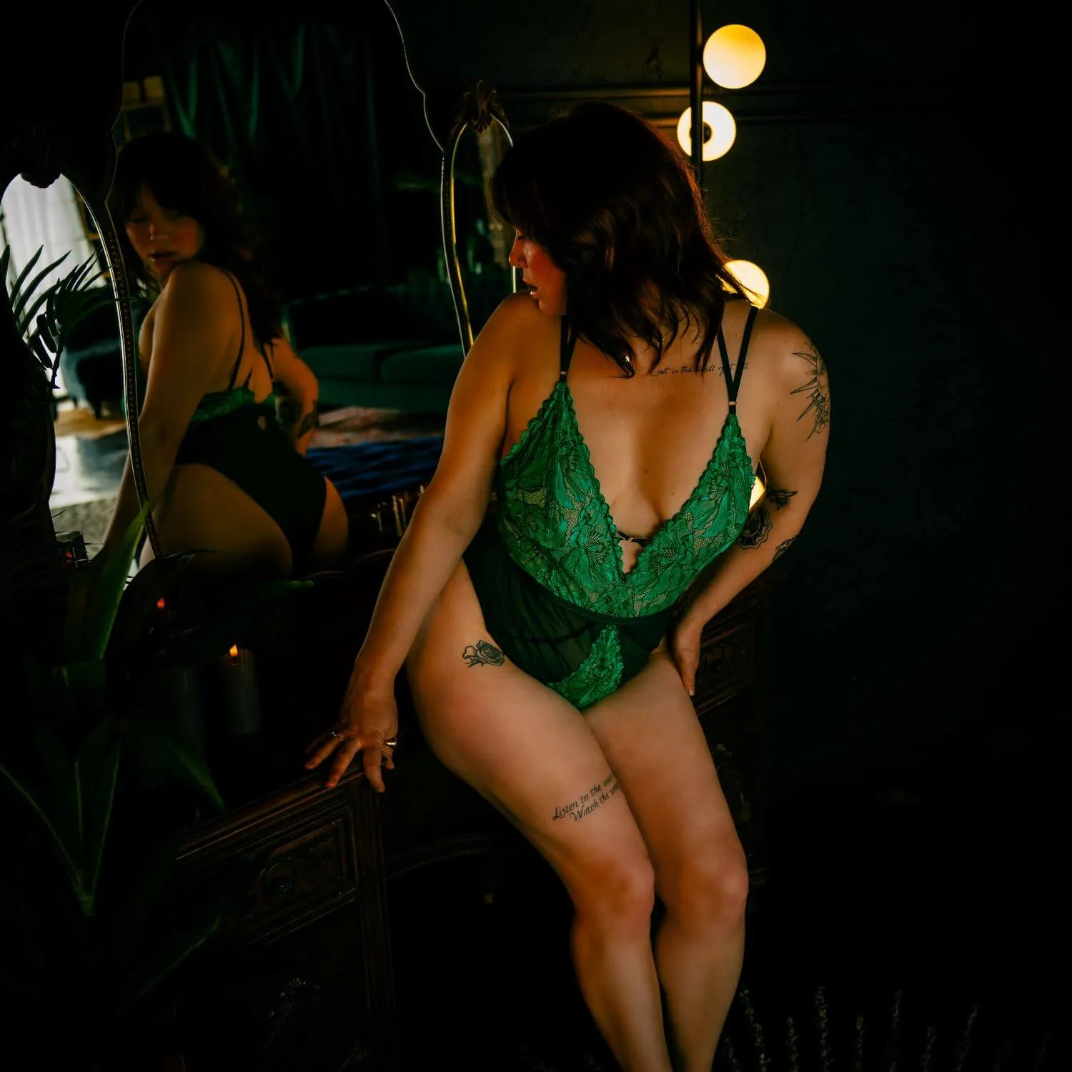 Woman in bold green lingerie, looking back at her reflection on the mirror behind her. 