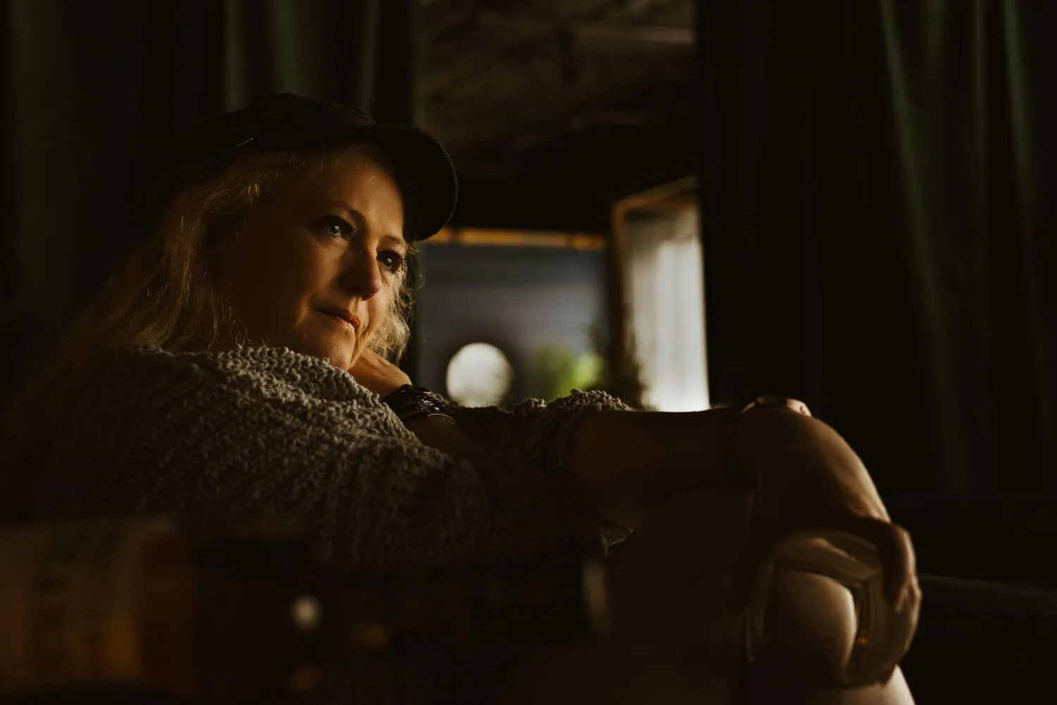 Blonde Senior in baseball cap, gazing off camera, empty glass in hand.