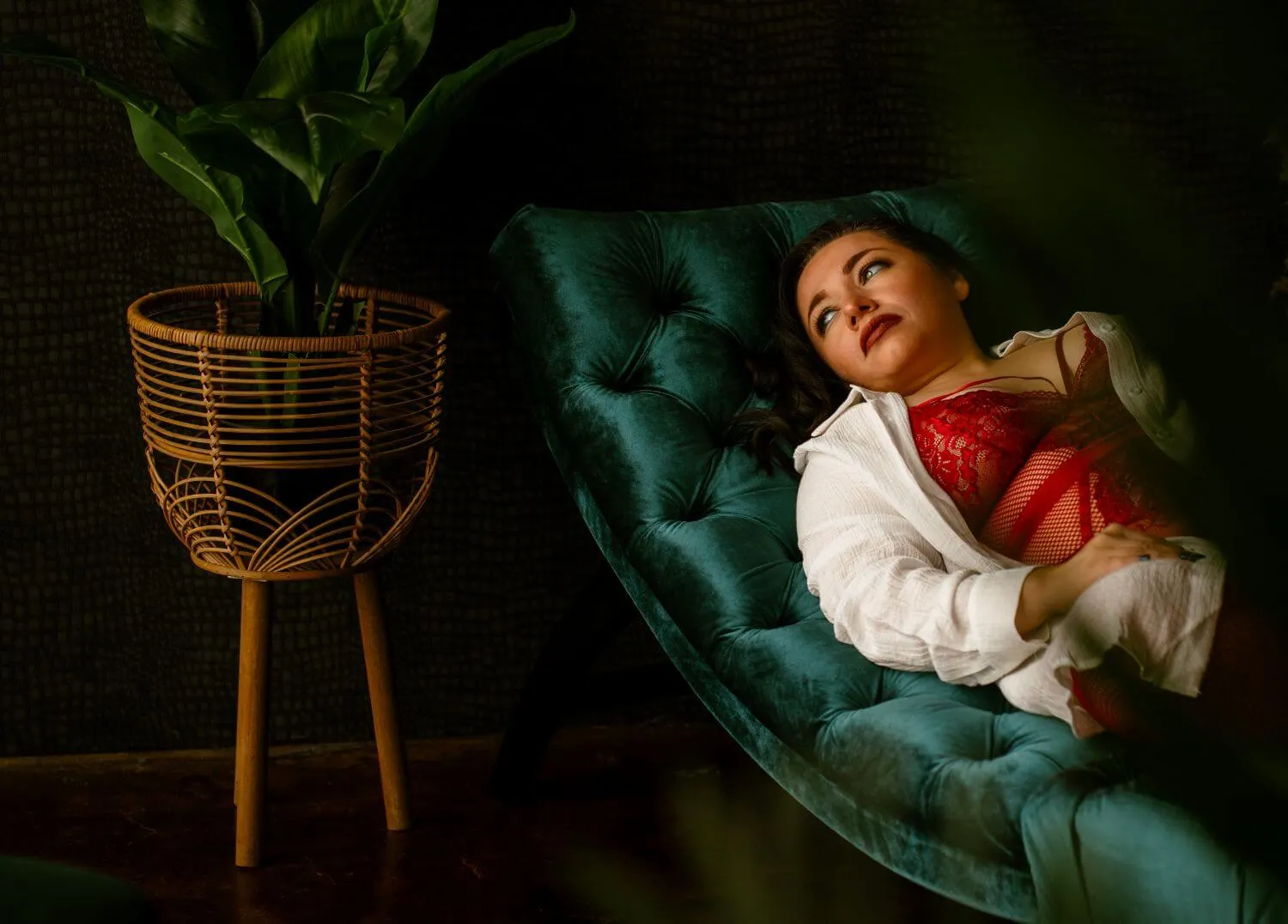 Woman lounging in red lingerie and white un-buttoned shirt, gazing off camera. 