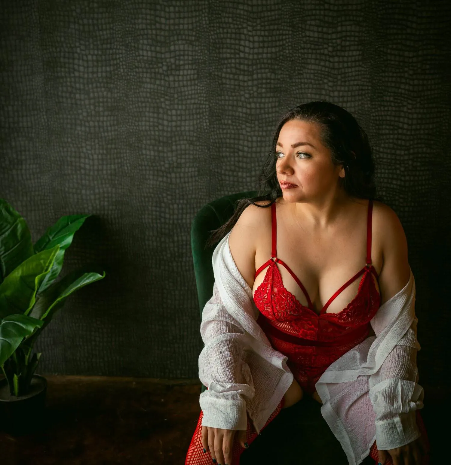 Confident woman leaning forward on chair in red lingerie, looking off camera. 