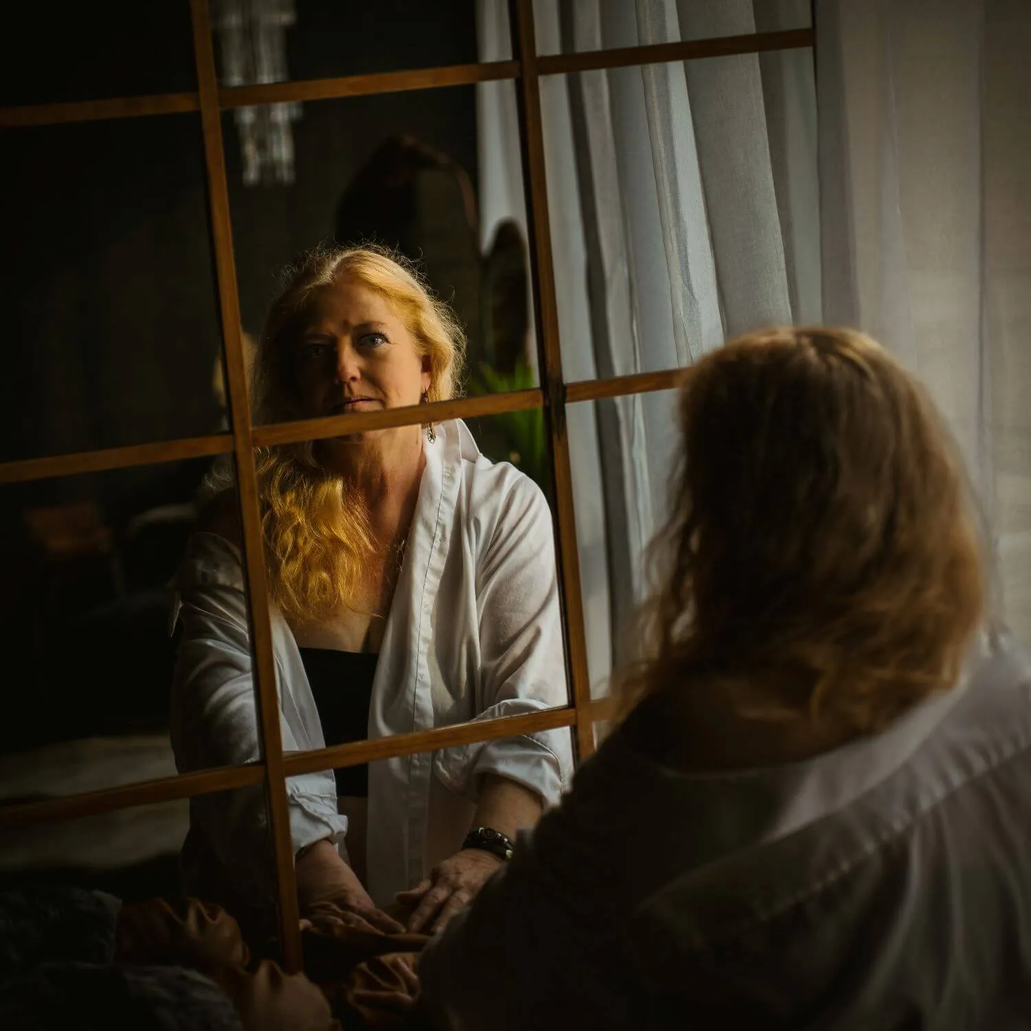 Mature blonde in white button-up gazing at camera through mirror reflection. 