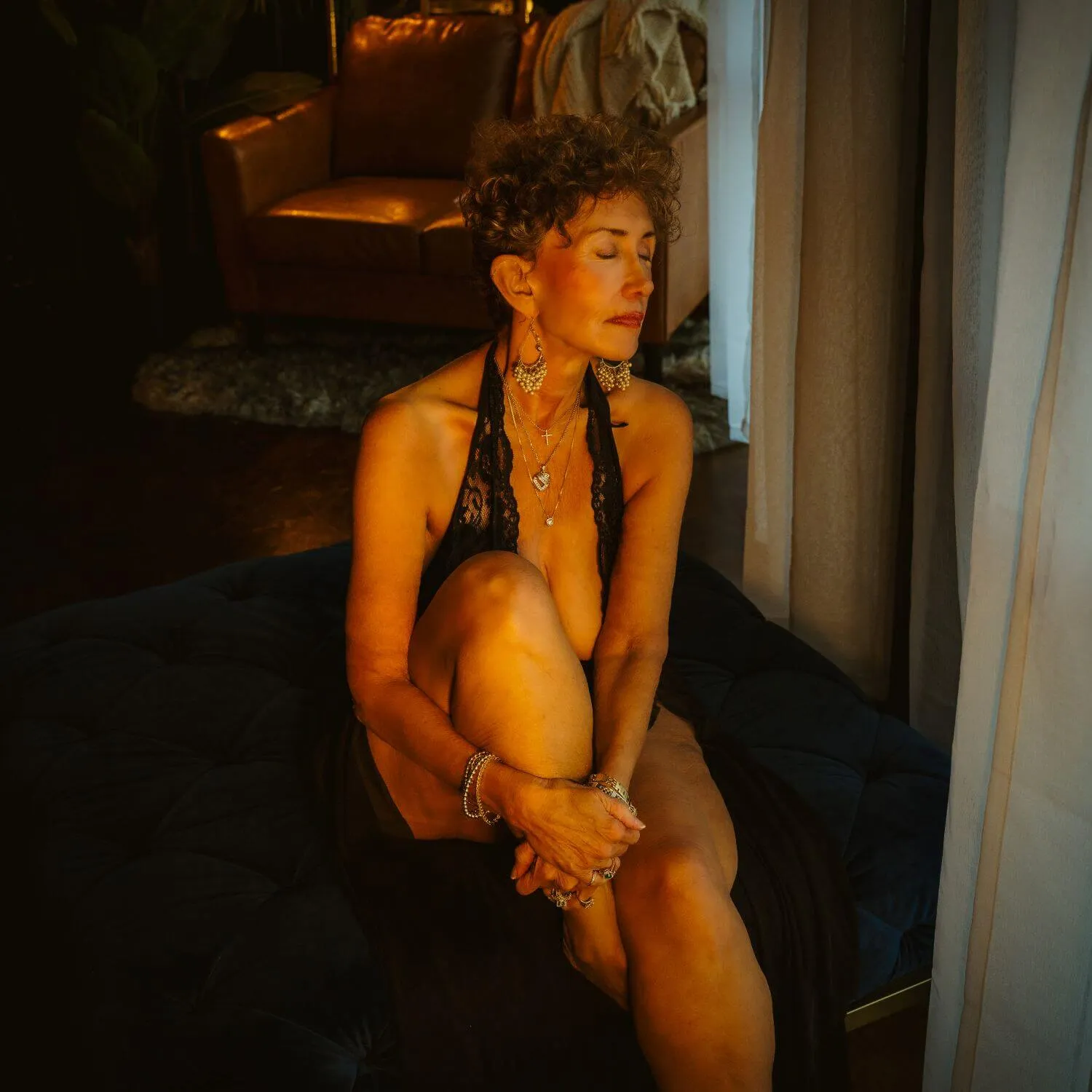 Empowered senior, eyes closed, posing with knee up in black lingerie. 