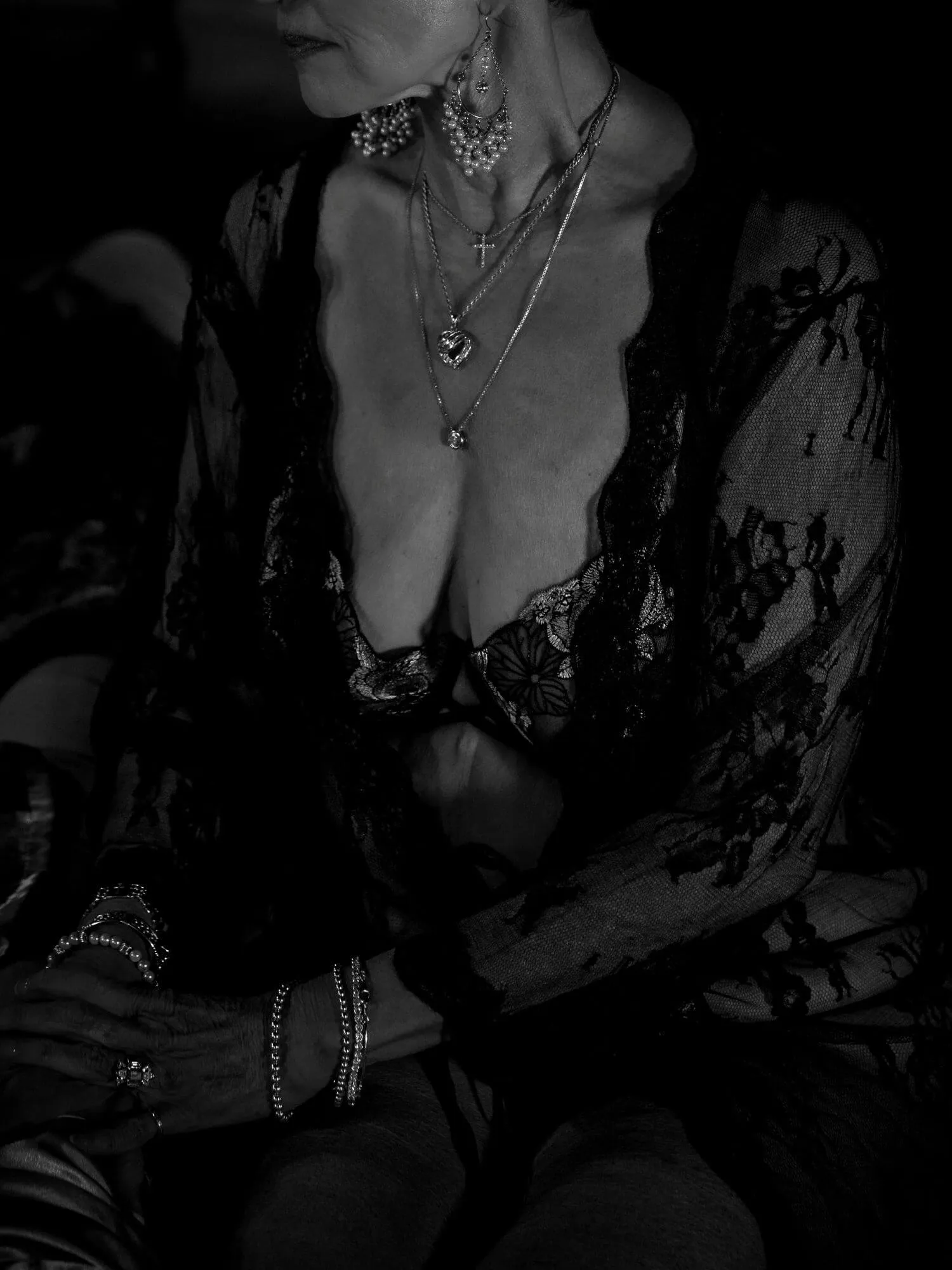 Senior woman sitting gracefully in black, sheer lingerie, adored with various shining pieces of jewelry.
