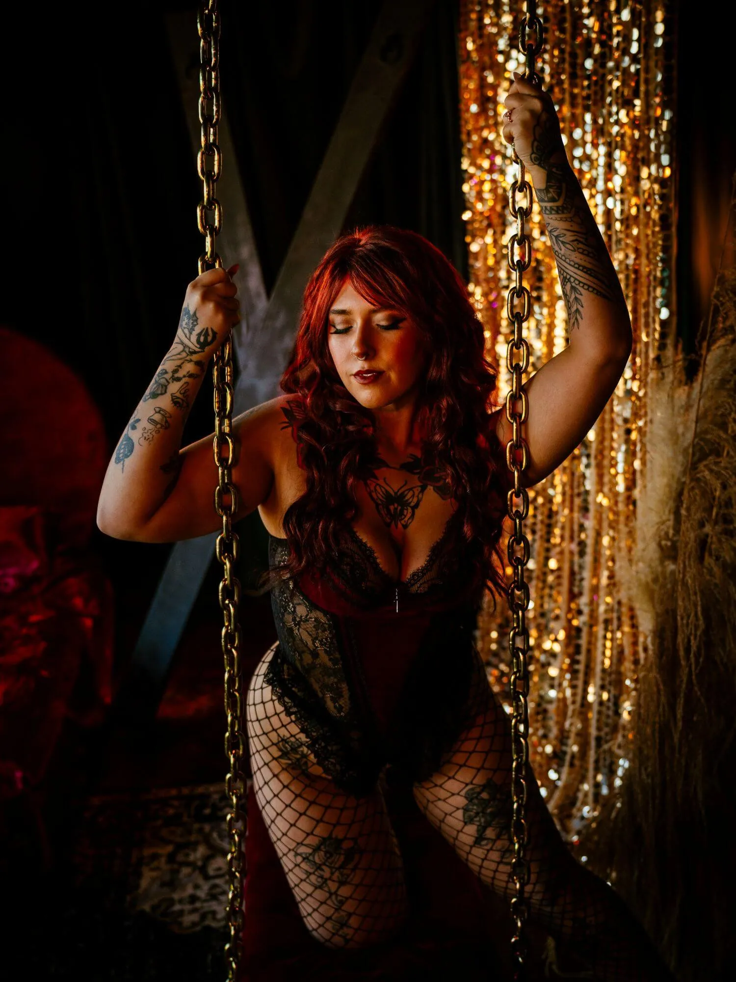 Tattooed woman posing with golden chains in black and red laced lingerie. 