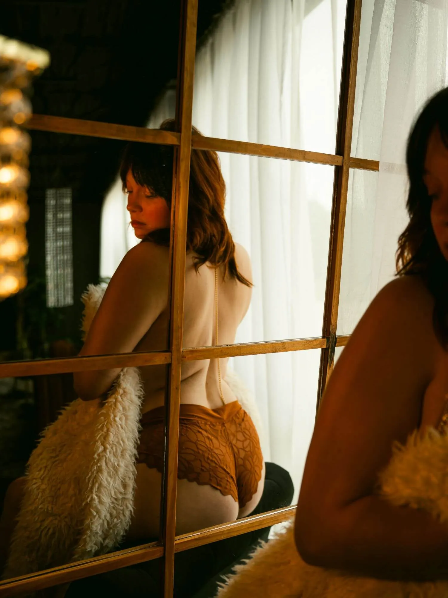 Mirror reflection of topless woman, covering herself with fur blanket, looking over shoulder.