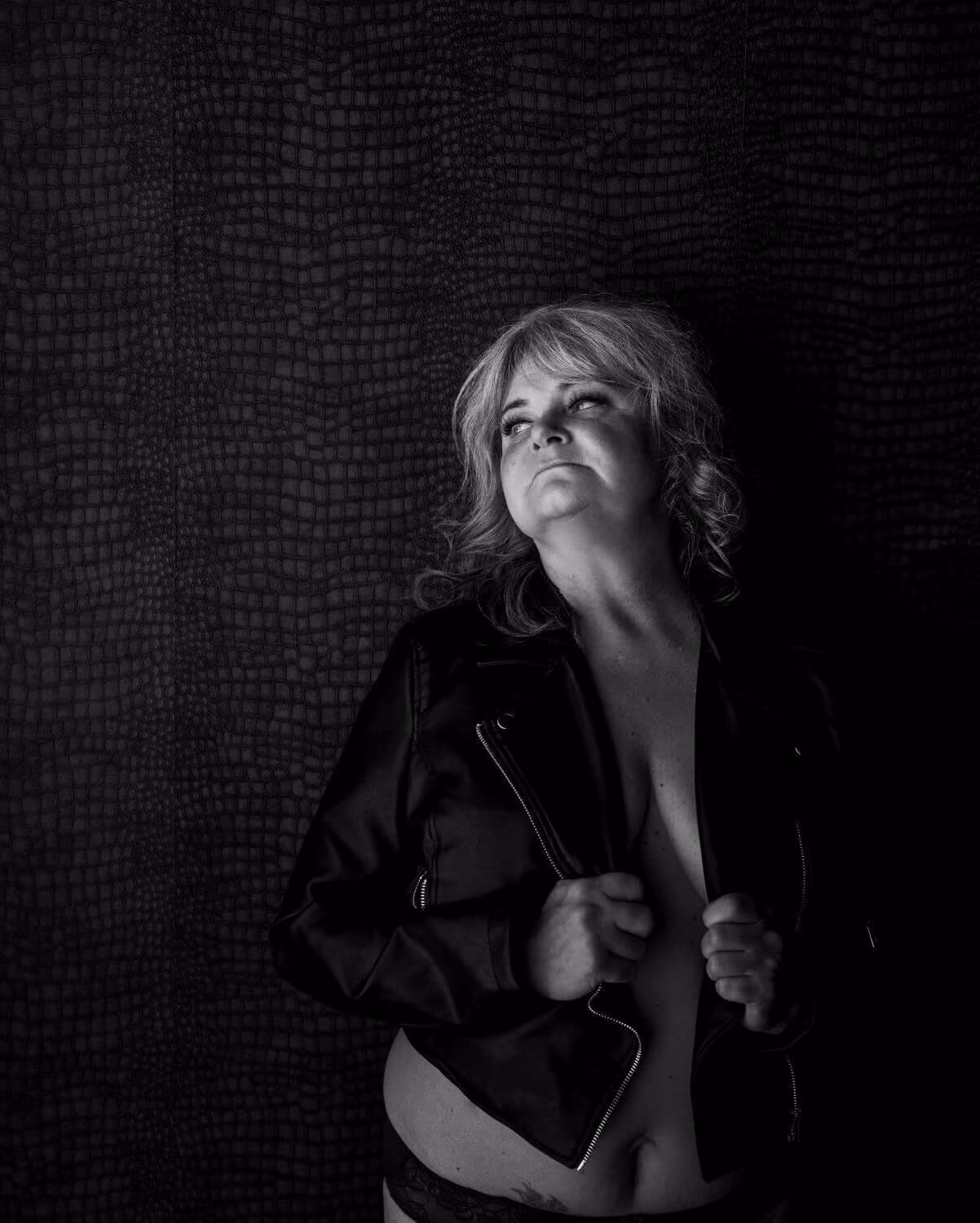 Mature woman in an open black leather jacket, gaze off camera, warm light.