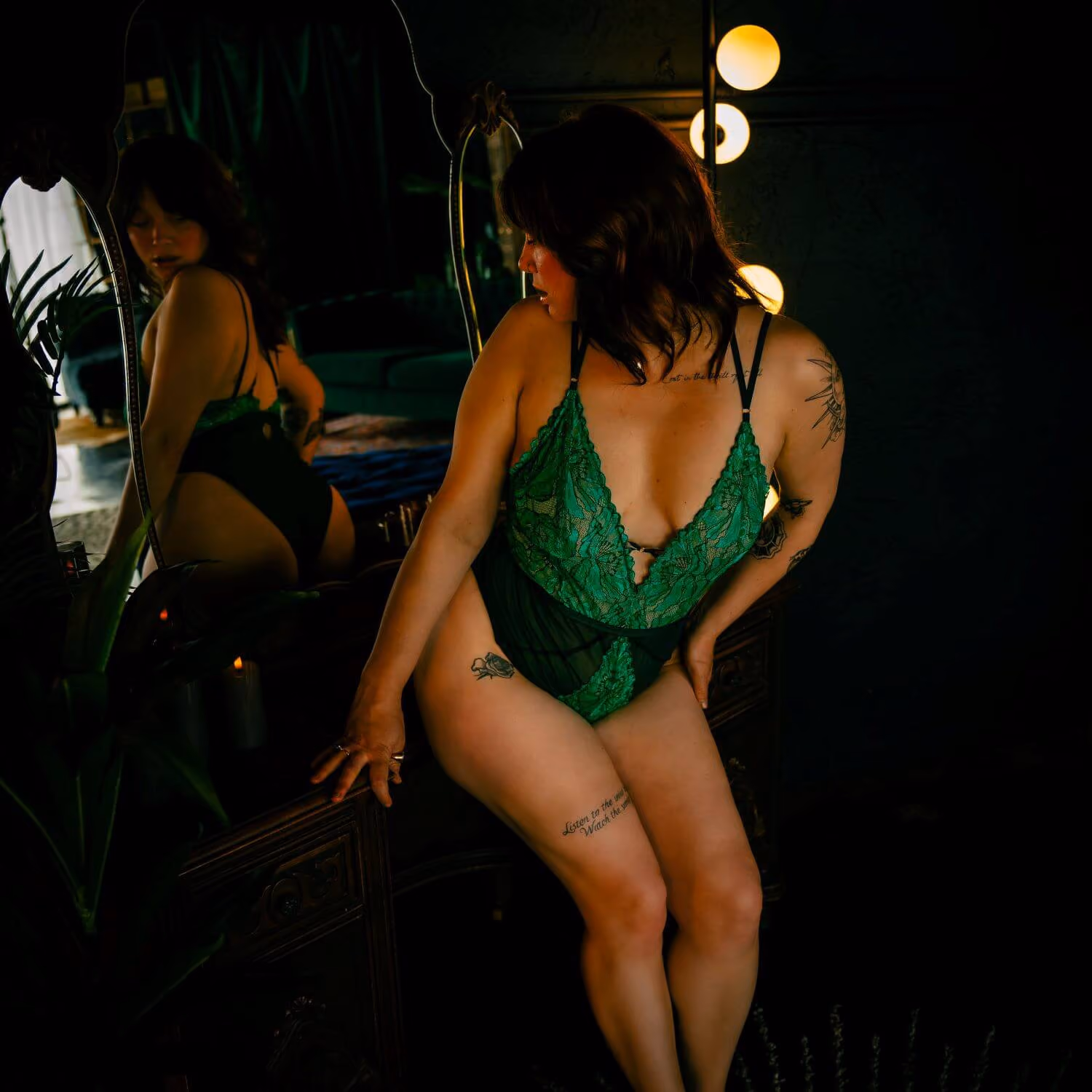 Woman in green lingerie looking back at her reflection in the mirror.