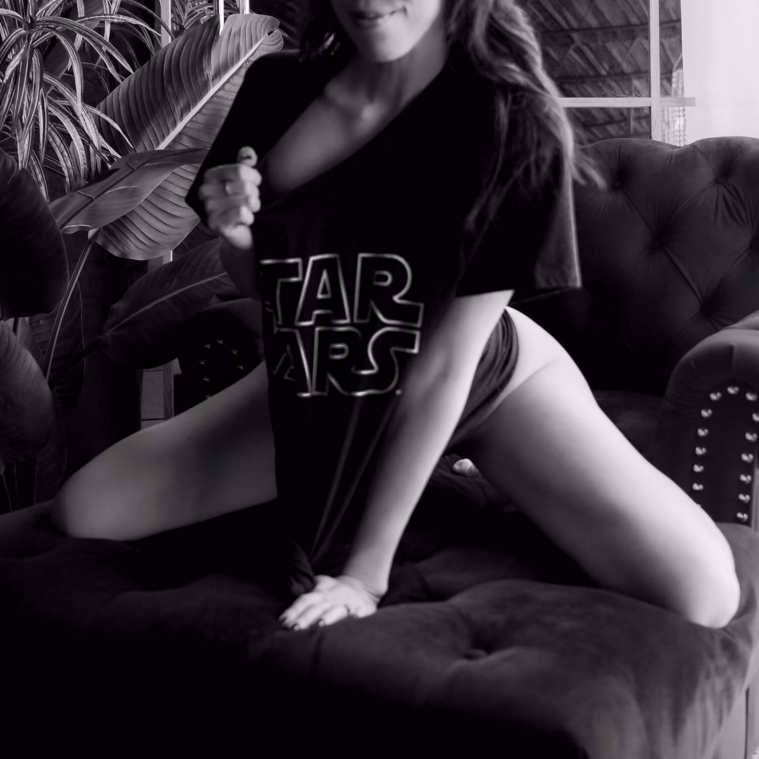 Woman kneeling, playfully tugging at a graphic t-shirt, black and white.