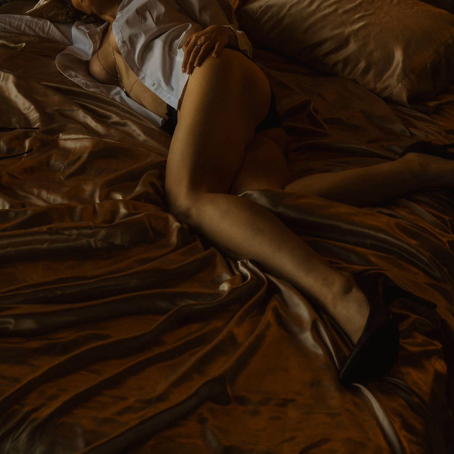 Woman on golden silk sheets in an unbuttoned shirt and heels.