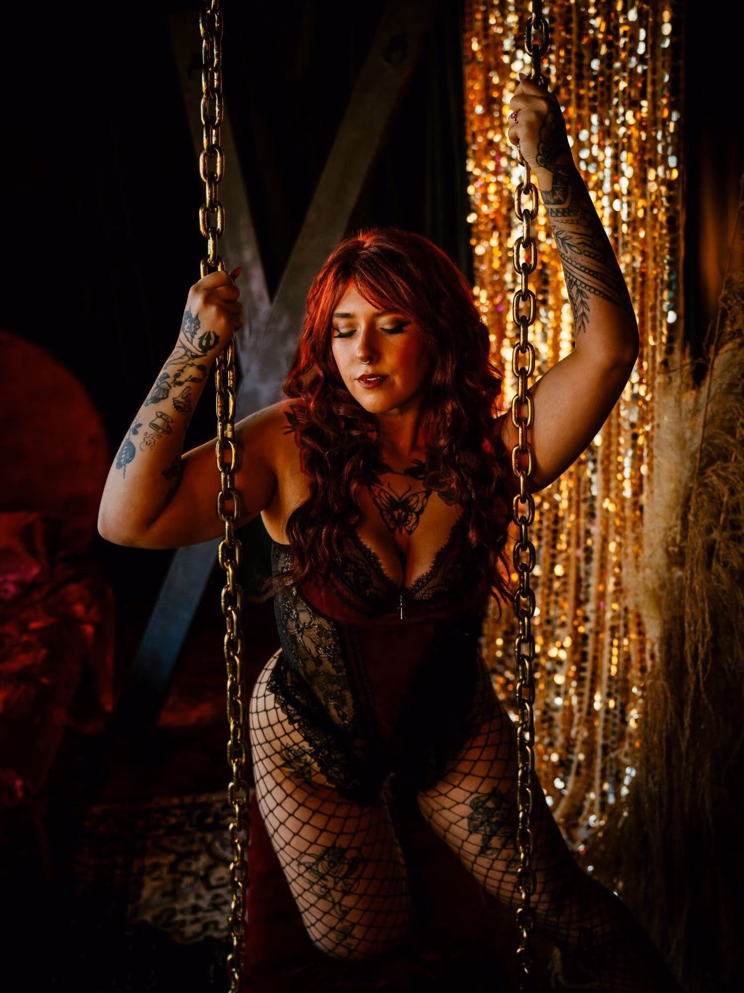 Tattooed woman posing with golden chains in black and red laced lingerie.