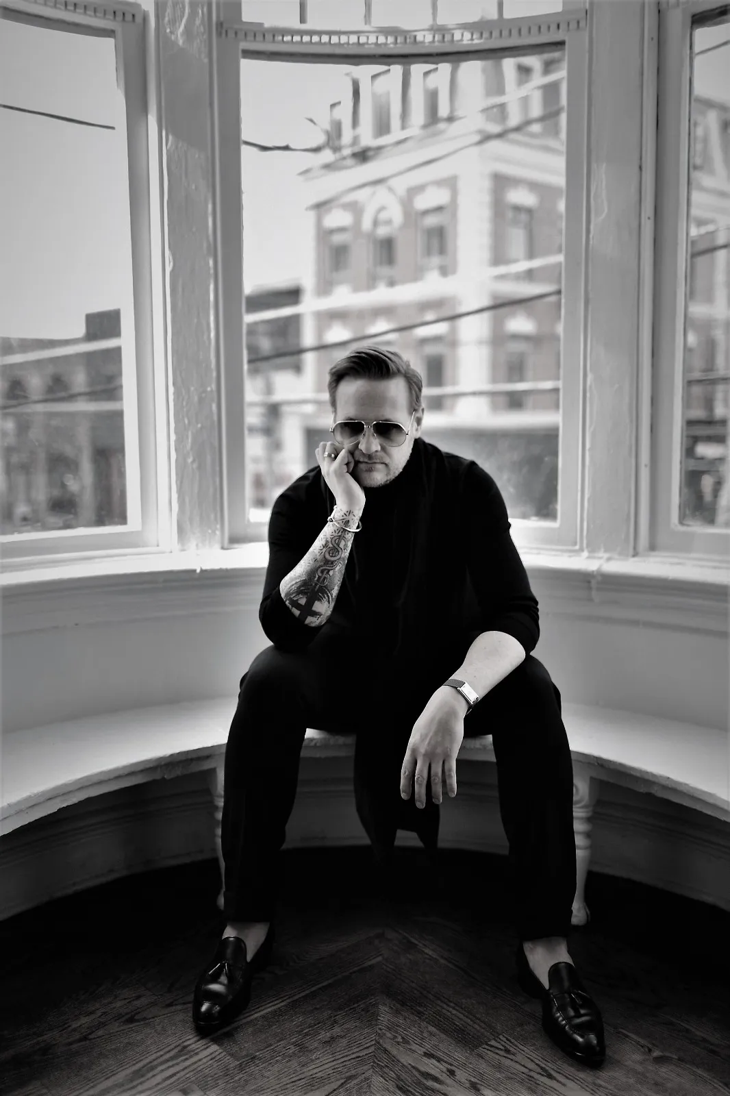 A photo of Matthew waering sunglasses siting  a curvy room with glass window