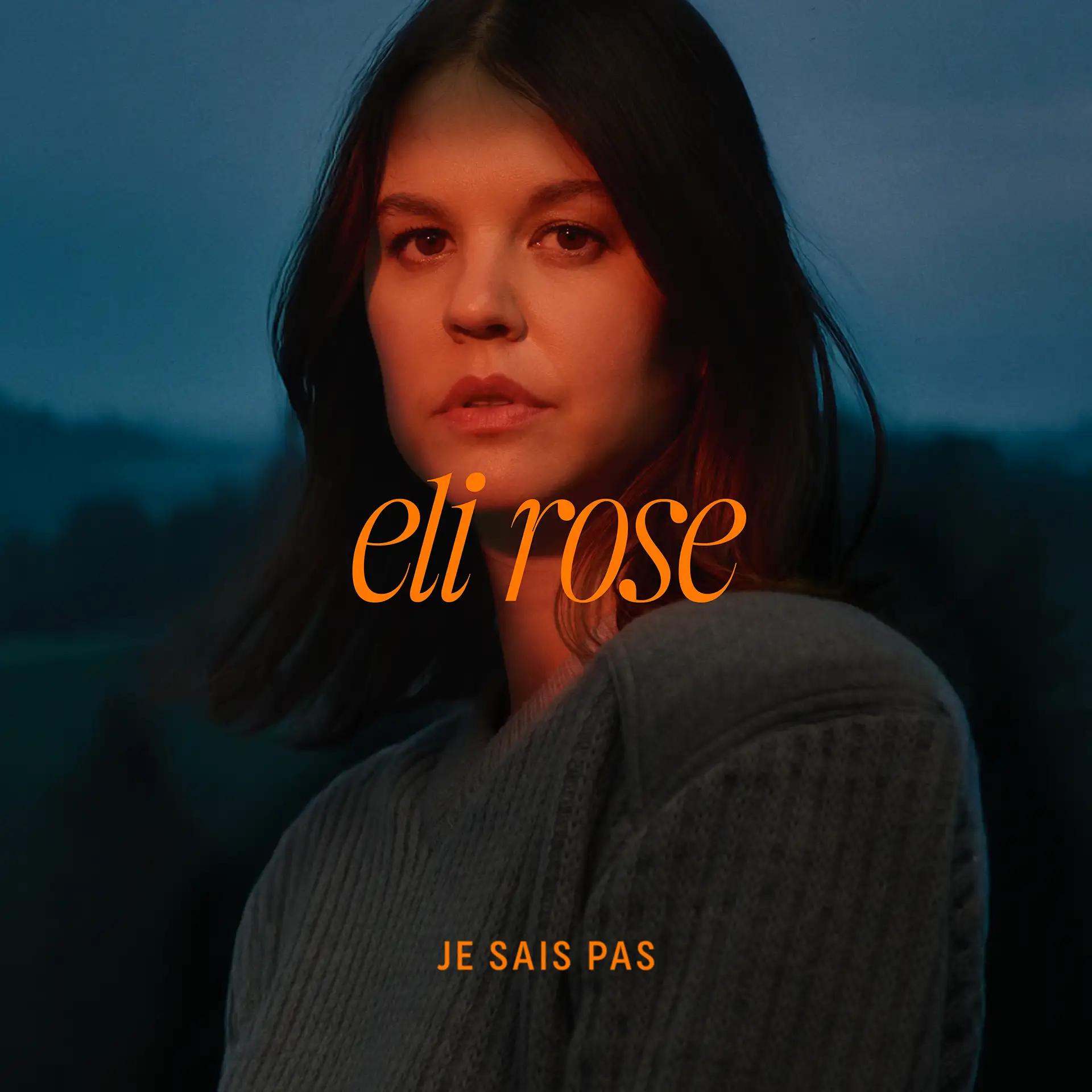 Portrait of Eli Rose under dusk lighting, with warm orange and cool blue tones creating contrast. The title “je sais pas” and the artist’s name appear in bold orange text. Portrait d’Eli Rose sous un éclairage crépusculaire, où les tons orange chaud et bleu froid créent un contraste marqué. Le titre “je sais pas” et le nom de l’artiste apparaissent en orange vif.