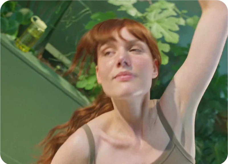 Alt text (EN / FR): A woman stretches with eyes closed in soft sunlight, surrounded by green plants—capturing a moment of mindful movement. / Une femme s’étire les yeux fermés dans une lumière douce, entourée de plantes vertes — un instant de mouvement en pleine conscience.