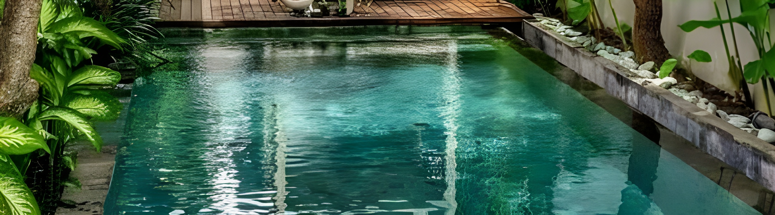 Discover Svasa Villa by Nurall.  Interiors include a cozy living room with beige sofa, a wooden coffee table with plants and books, and large sliding glass doors opening to a garden with a tree and plants.