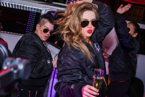 First preview with cast members (left to right) Lea DeLaria, Julianne Hough, and Suzy Nakamura all dancing outside limo with champagne, matching aviator sunglasses, and bomber jackets.