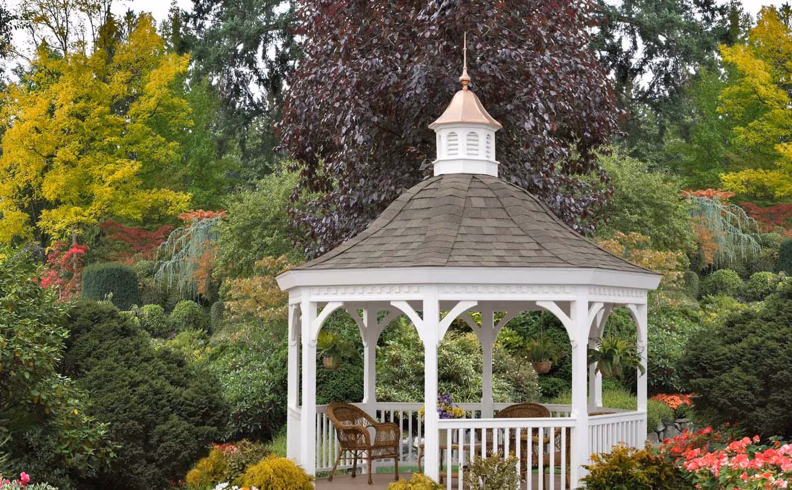 Decorative copper-topped gazebo cupola with louvered vents and finial, featured on a white garden gazebo surrounded by colorful landscaping.