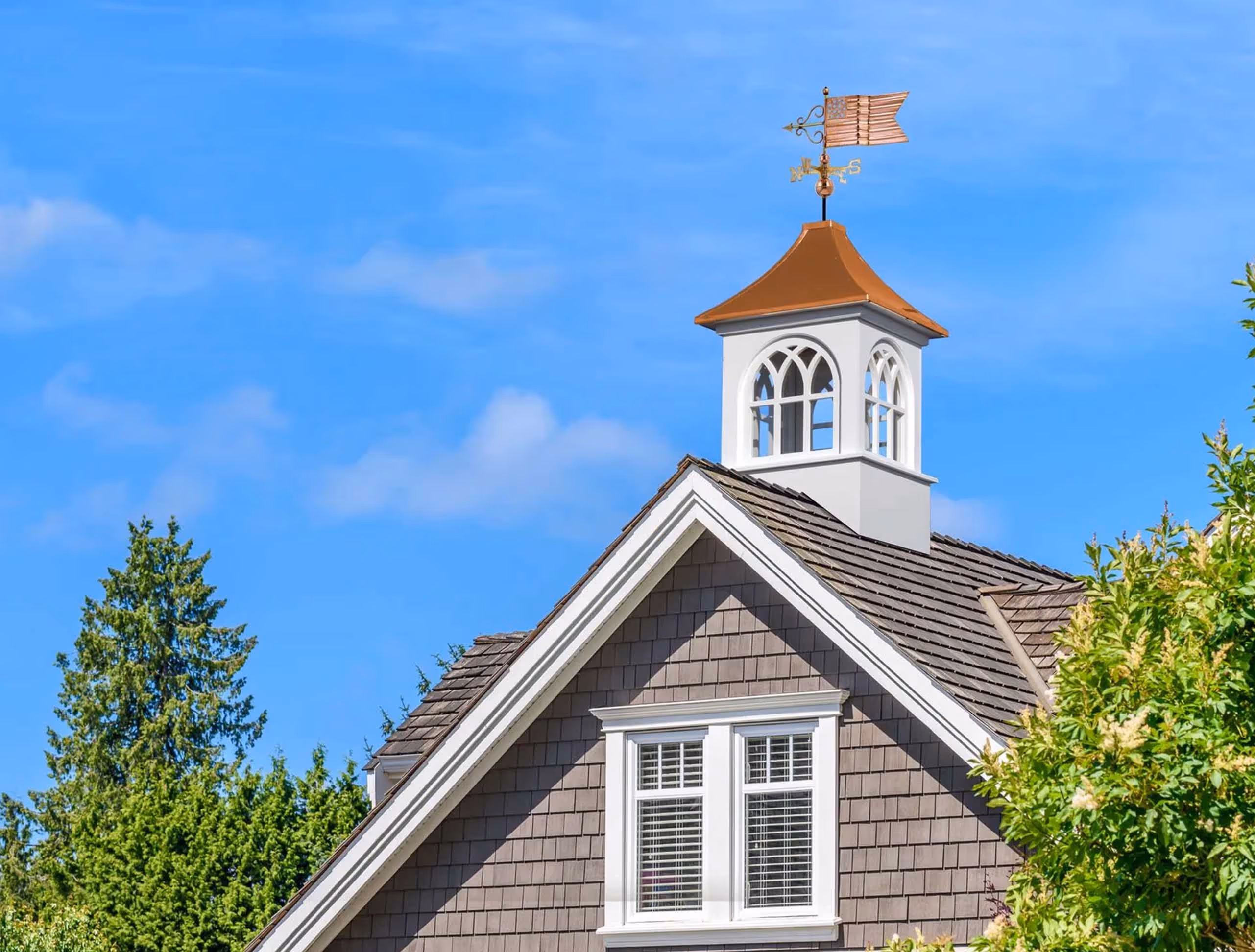 Decorative white Roxbury-style estate cupola with copper roof and American flag weathervane on a shingle roof home in Millersburg, OH.