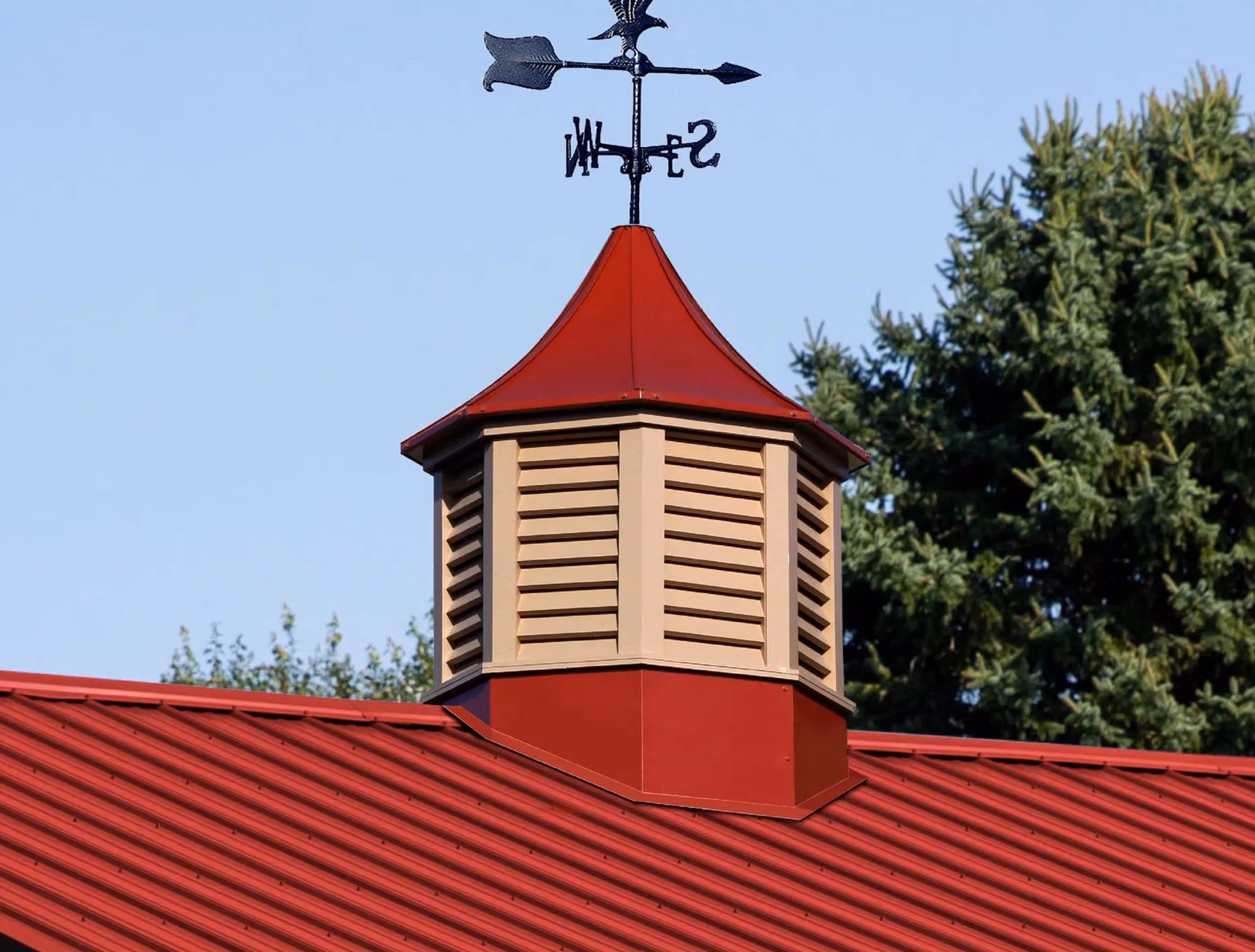 Red Salem-style Sundance cupola with beige louvers and directional arrow weathervane, mounted on a metal roof structure in Millersburg, OH.