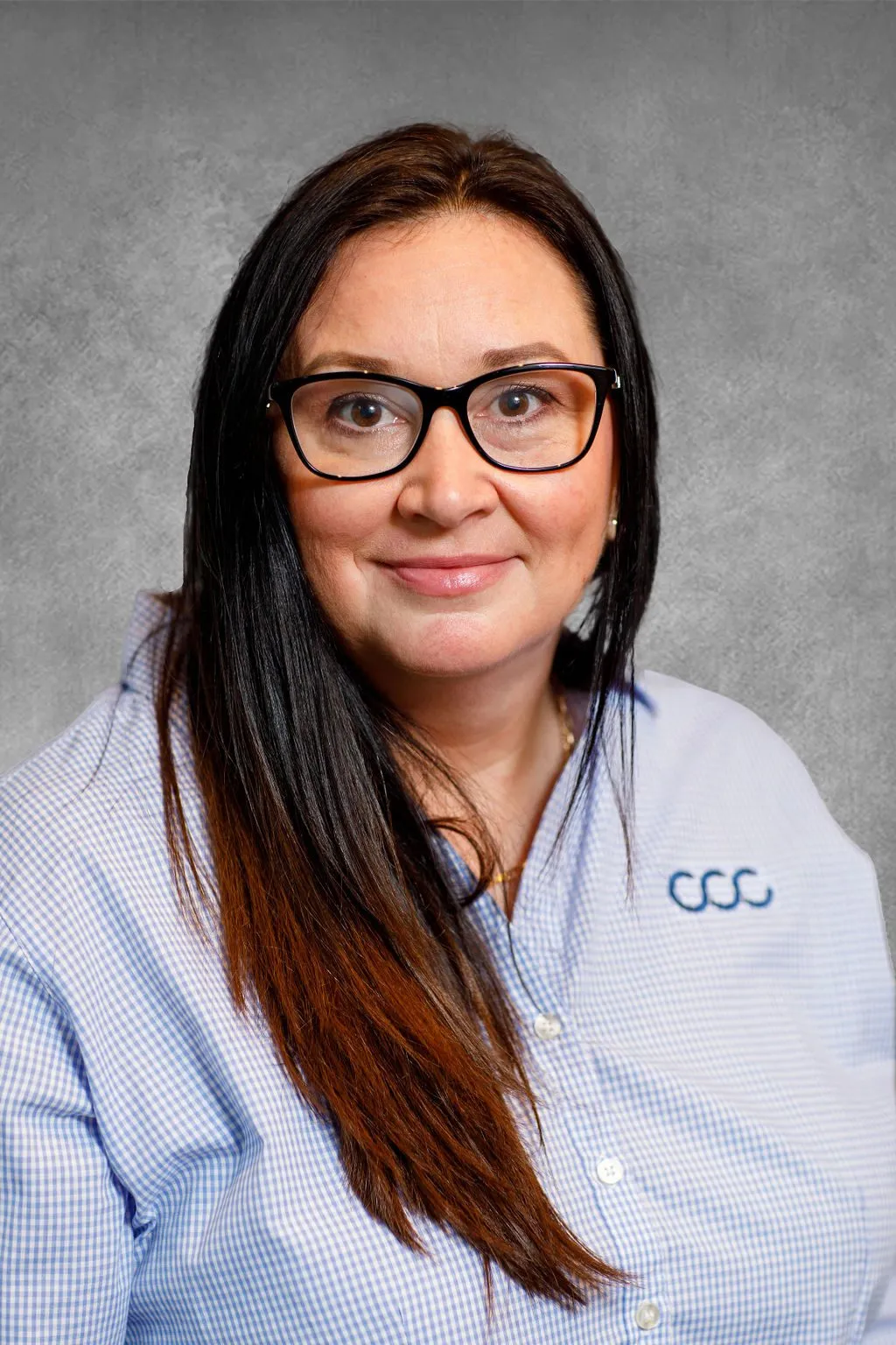 Woman with long dark hair and glasses wearing a light blue checkered shirt.