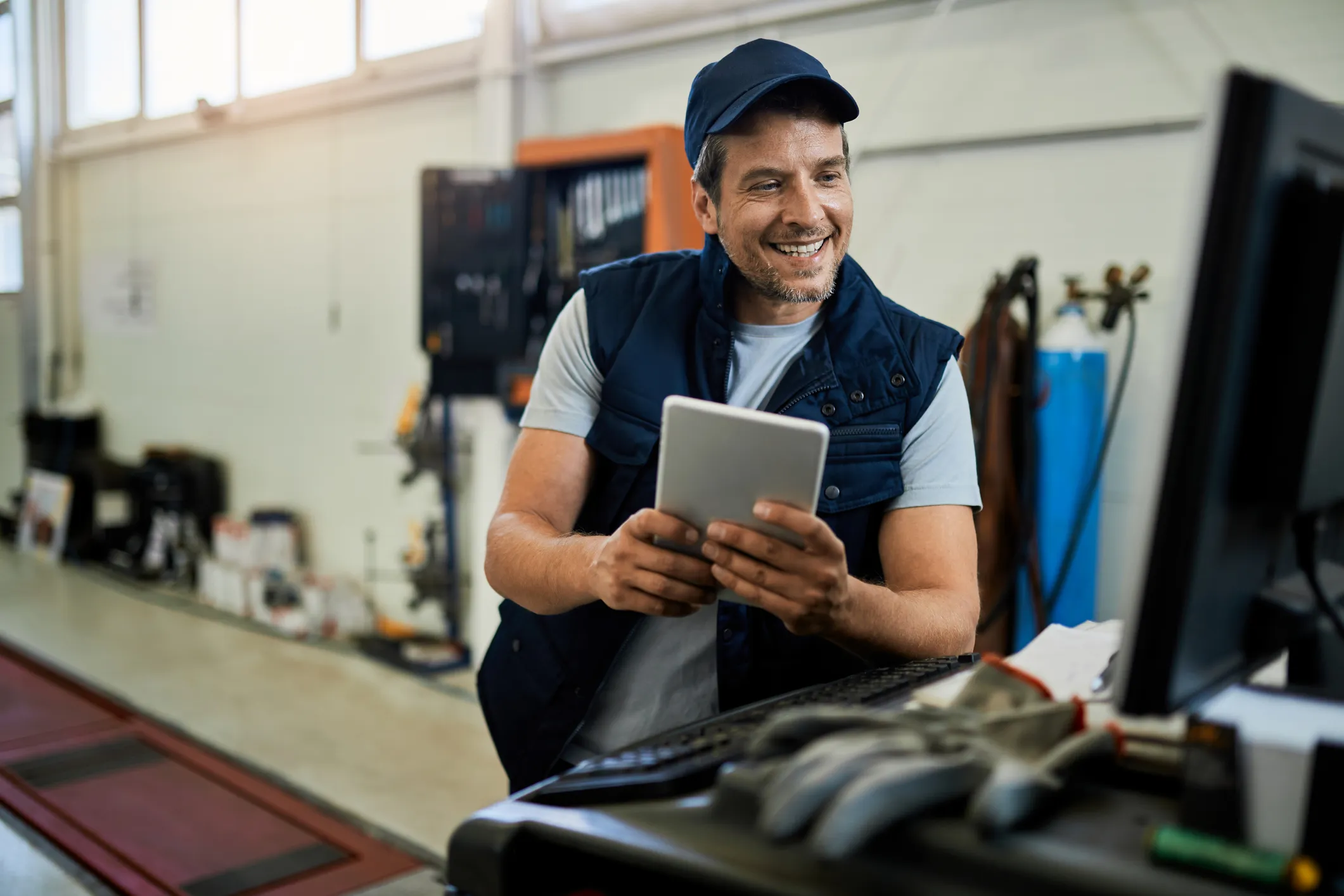 Smiling mechanic holding a tablet and looking at a computer screen in a workshop.