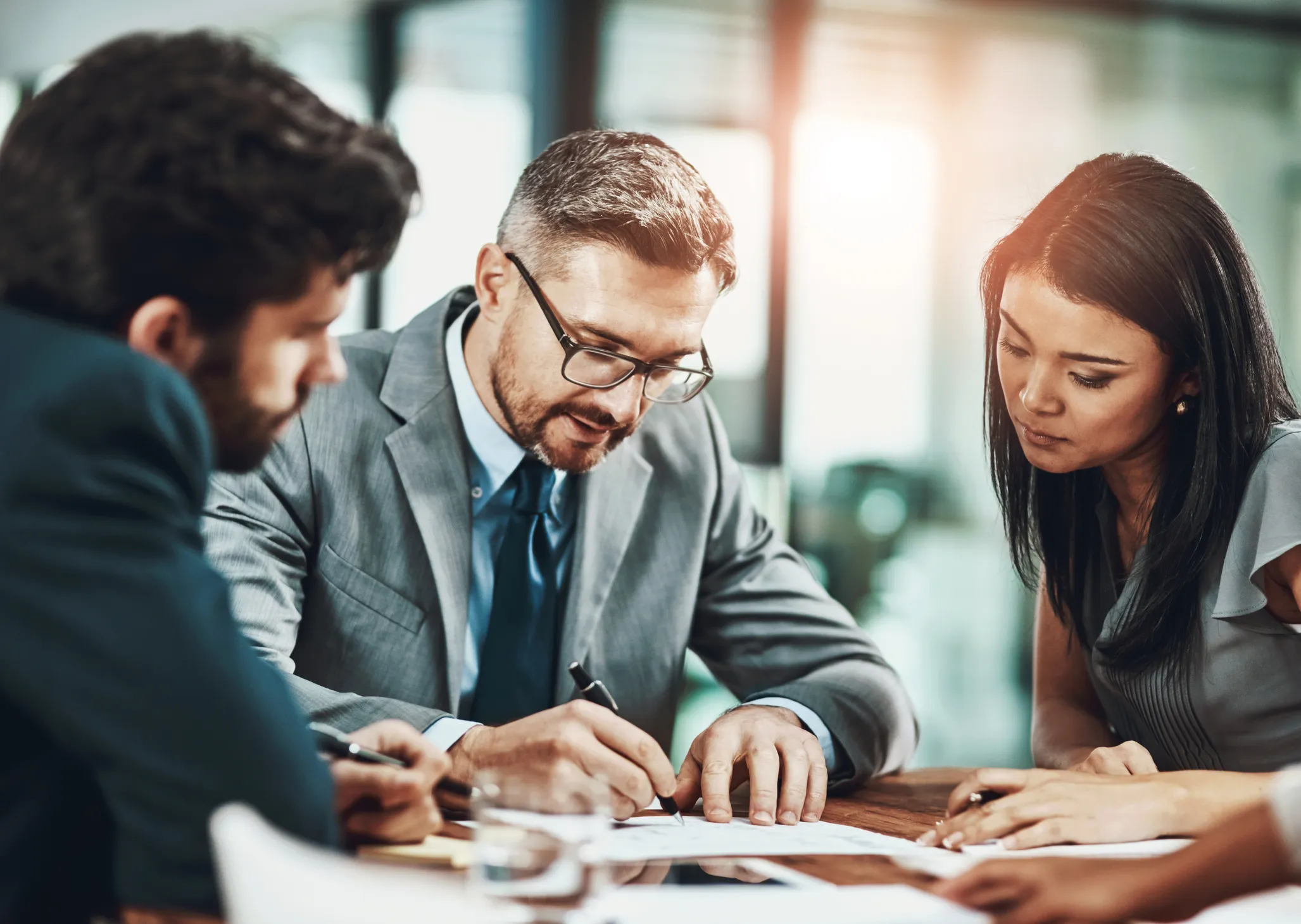 Three business professionals collaborating over documents at a desk in a modern office.