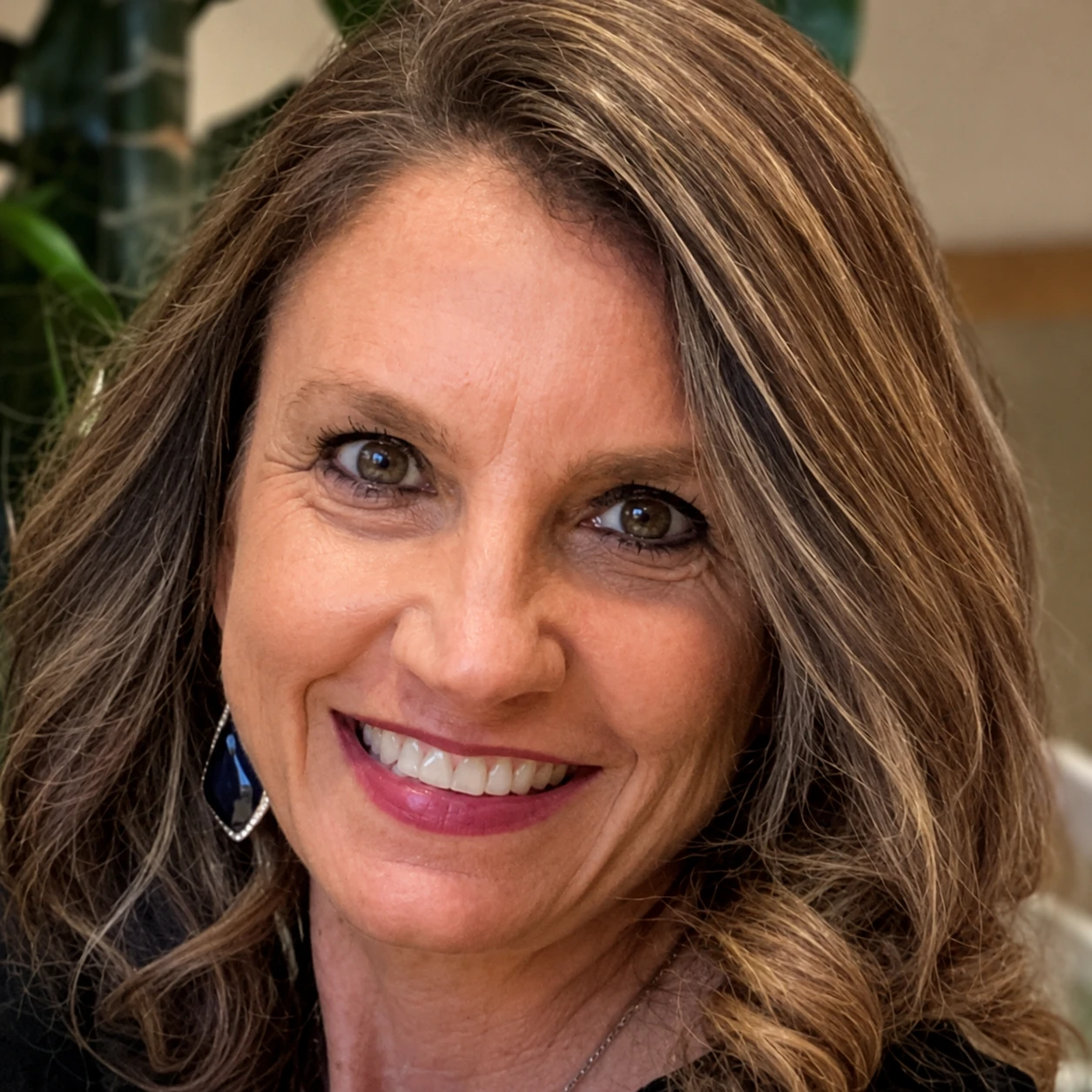 Close-up of a smiling woman with wavy highlighted hair and blue teardrop earrings.