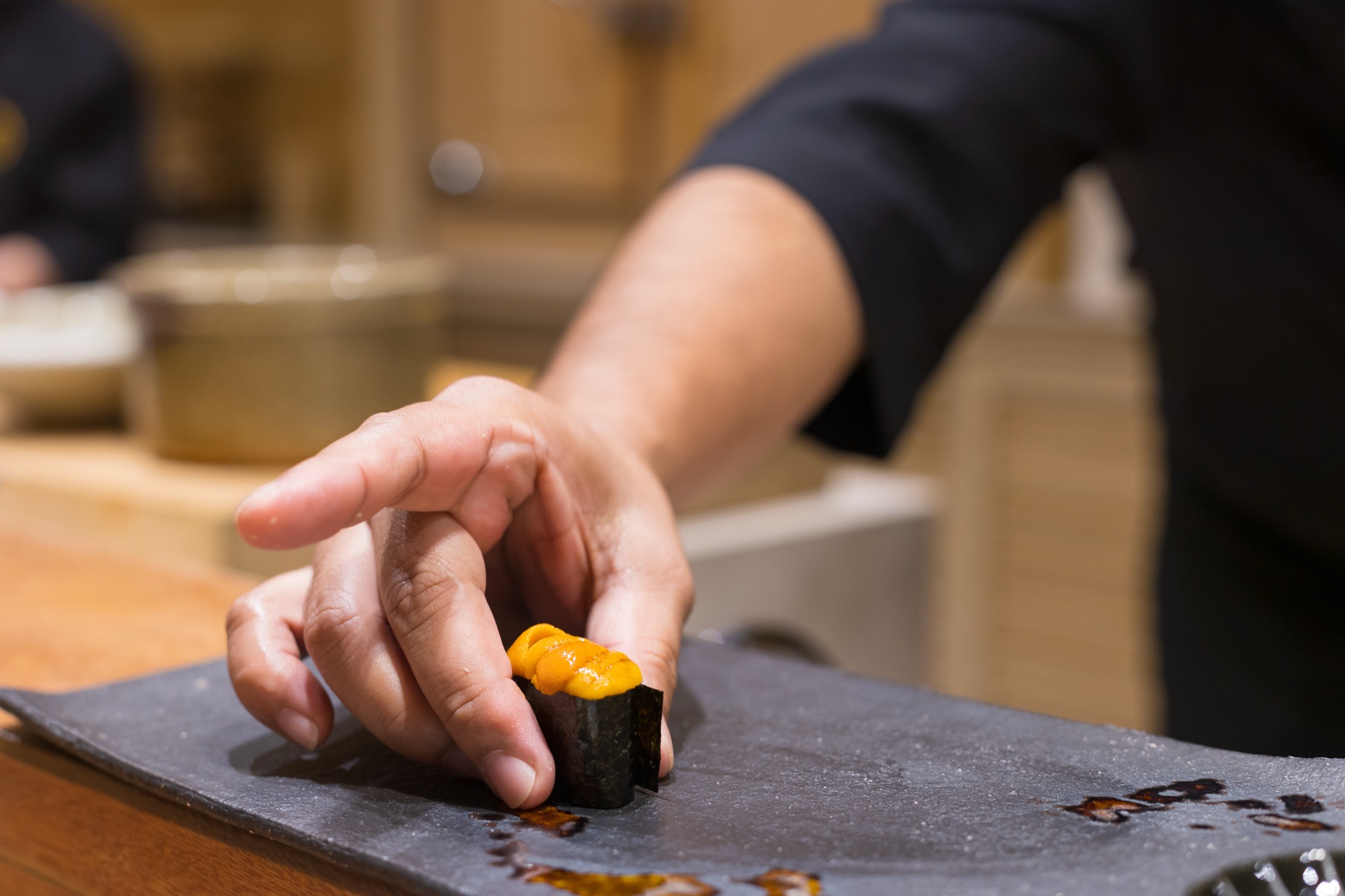 A sushi chef placing uni gunkan sushi on a stone plate