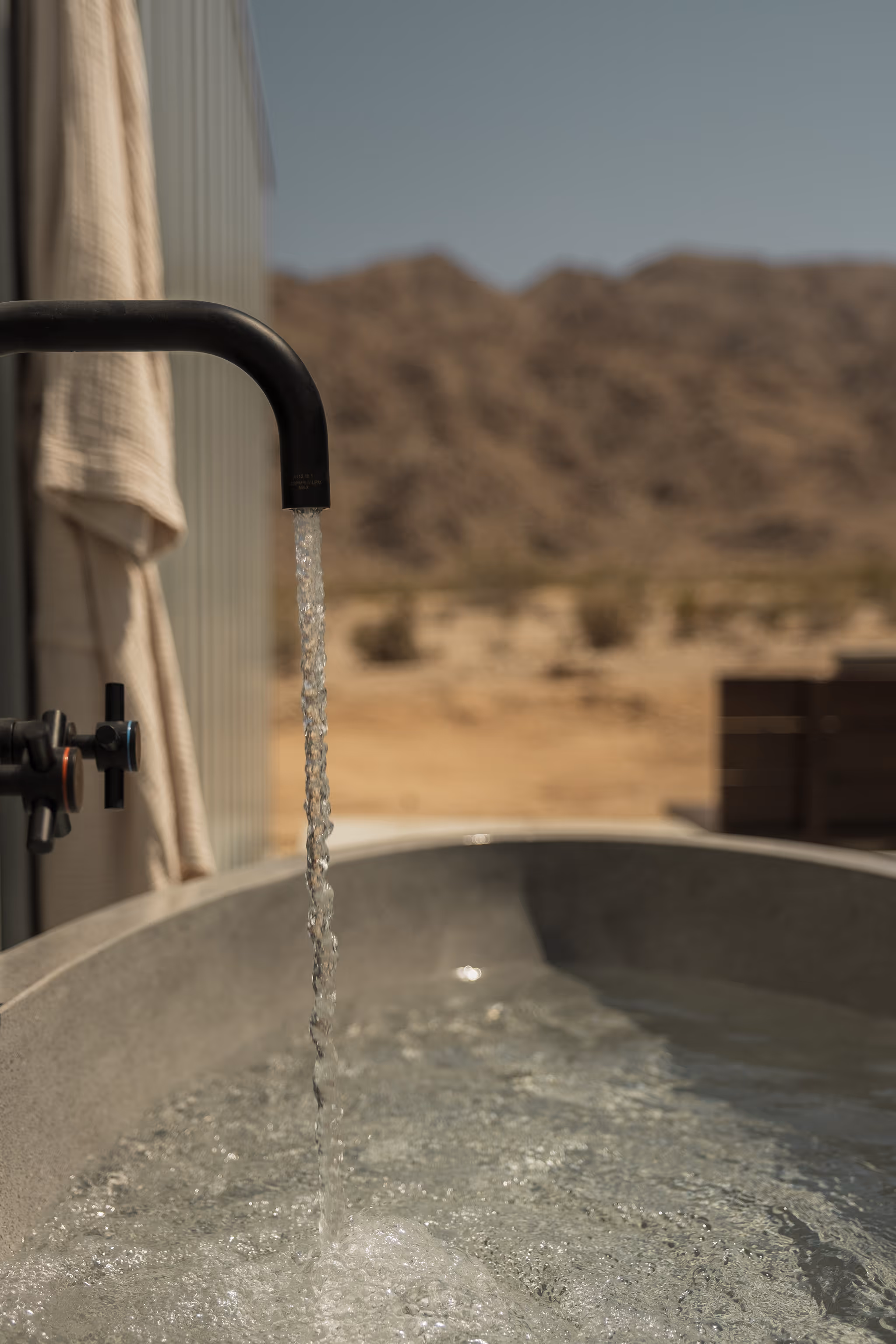 Tranquil water flowing from a black faucet into a concrete tub at Reset Hotel, Twentynine Palms