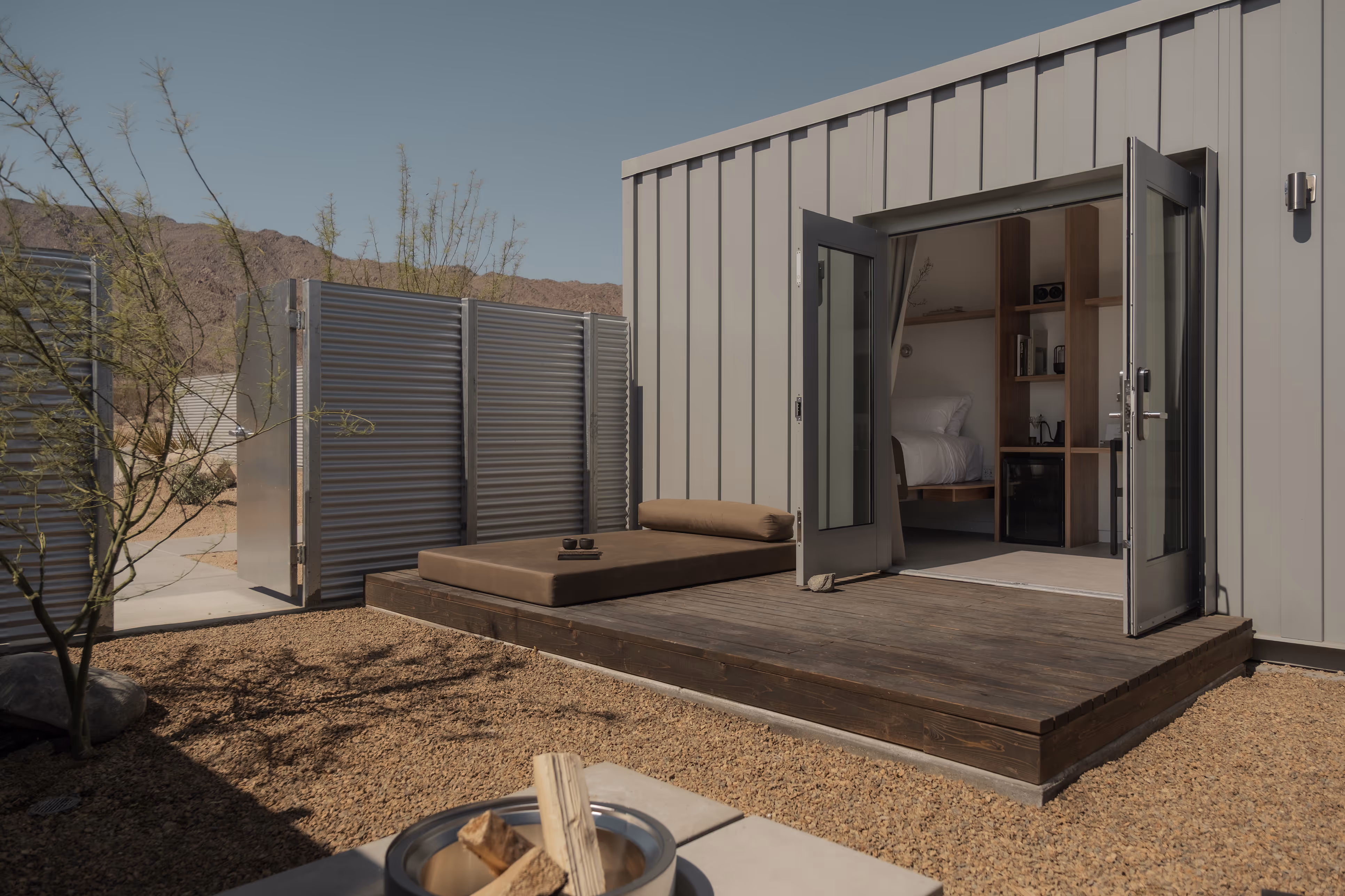 Modern minimalist cabin with open doors, deck daybed, and desert view at Reset Hotel, Twentynine Palms