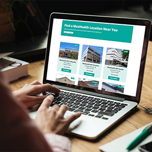 Person using a laptop displaying a webpage to find a MaxHealth location nearby, showing multiple location options with images and addresses.