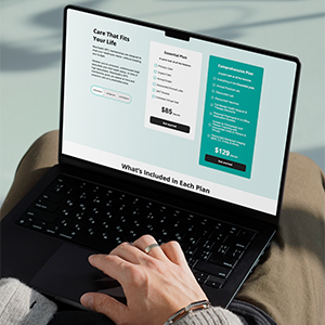 Person's hand using a laptop displaying a comparison of essential and comprehensive care plans with prices and features.