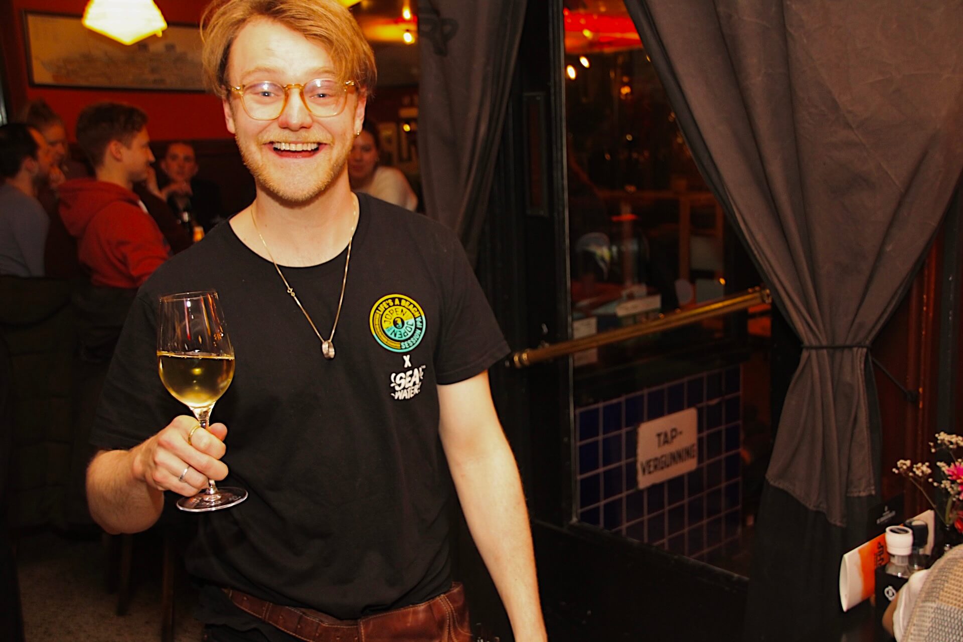 Iemand van de bediening van Verhip die met een brede glimlach een wijntje naar een tafel brengt