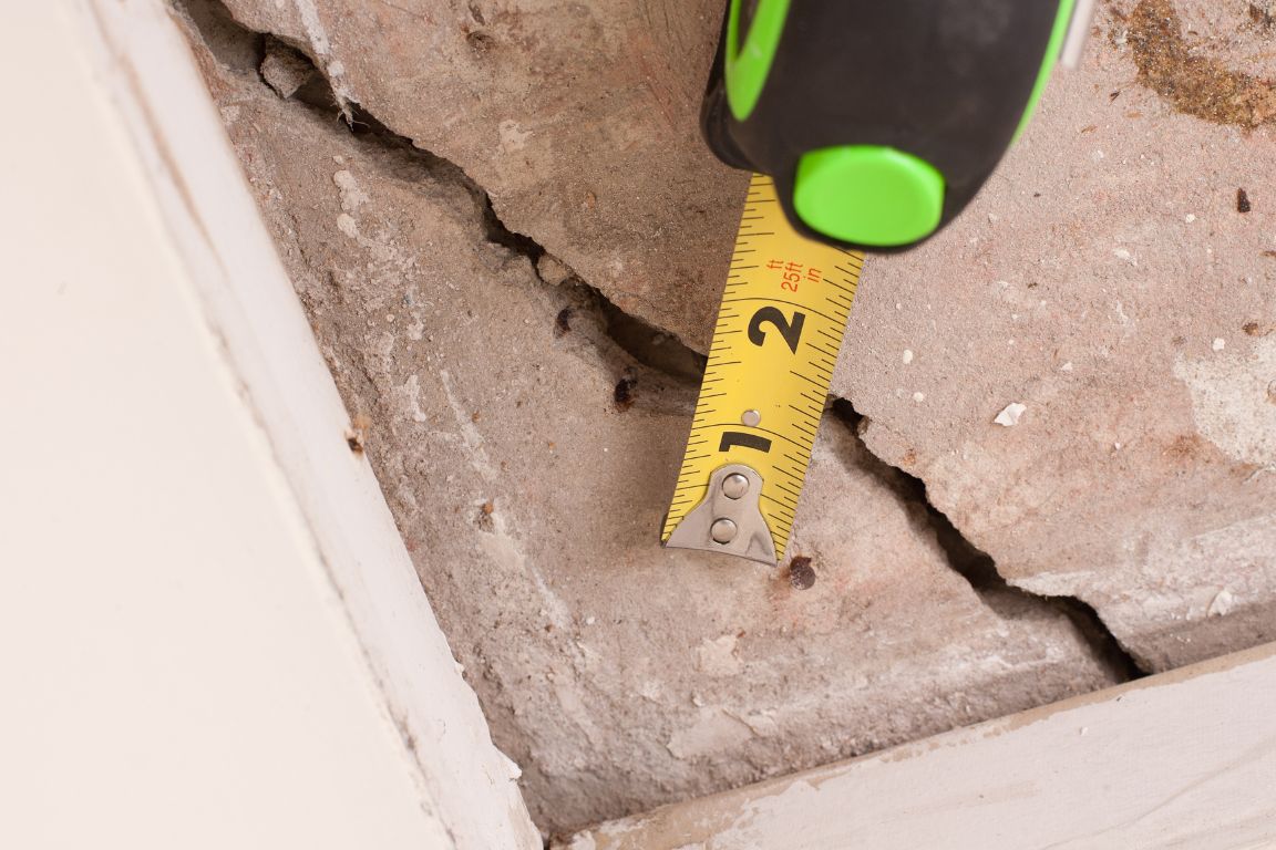 measuring width of crack in slab foundation with measuring tape