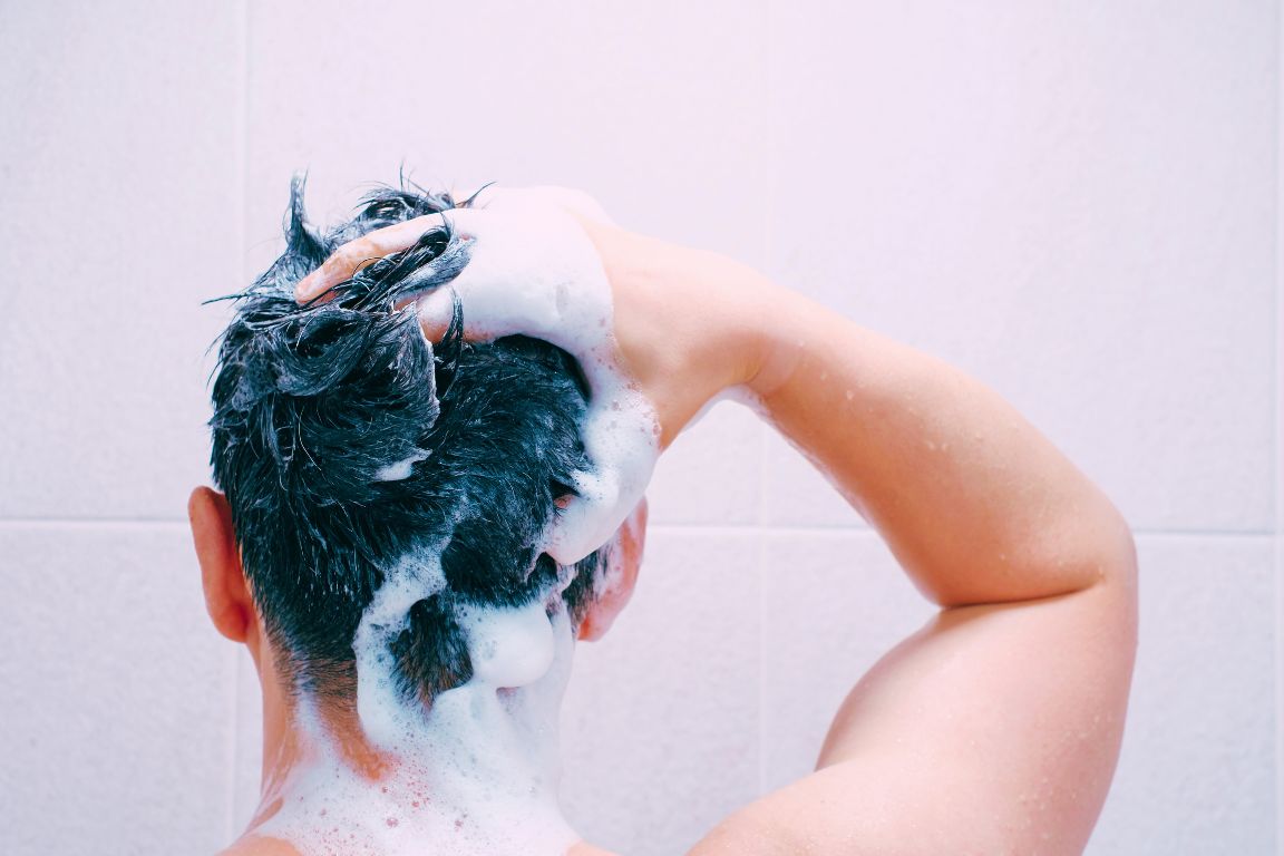 man uses sulfate free shampoo in shower to maintain natural oils