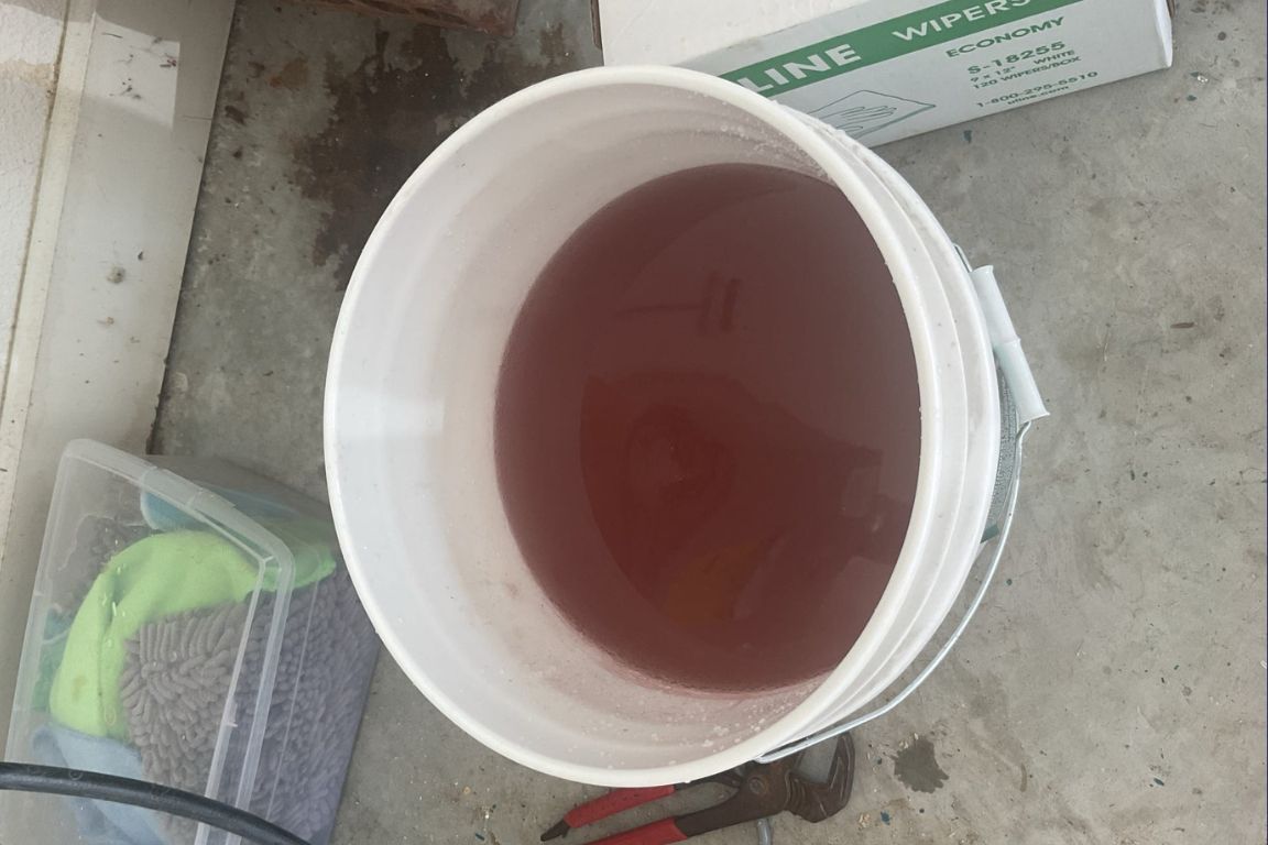 bucket of rust-colored water collected from conventional water heater with sediment buildup, mother modern plumbing