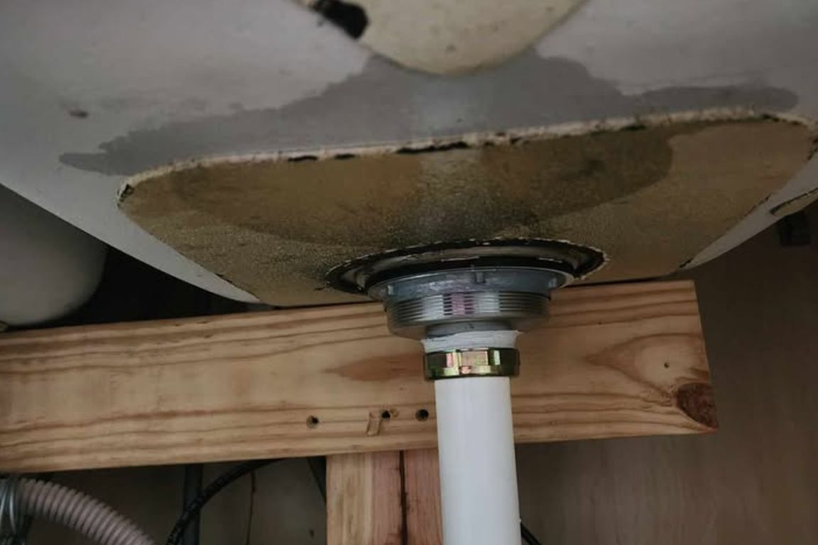 under kitchen sink damage from months of grease clog buildup