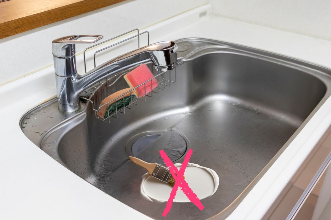 wet paintbrush with white paint in sink, illegal to pour paint down the sink drain