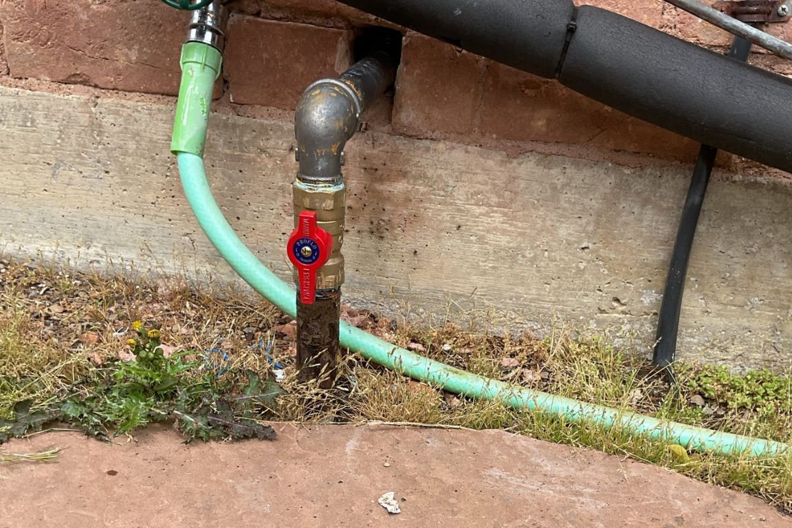 close up of black iron gas supply line entering home through exterior wall with red valve, mother modern plumbing