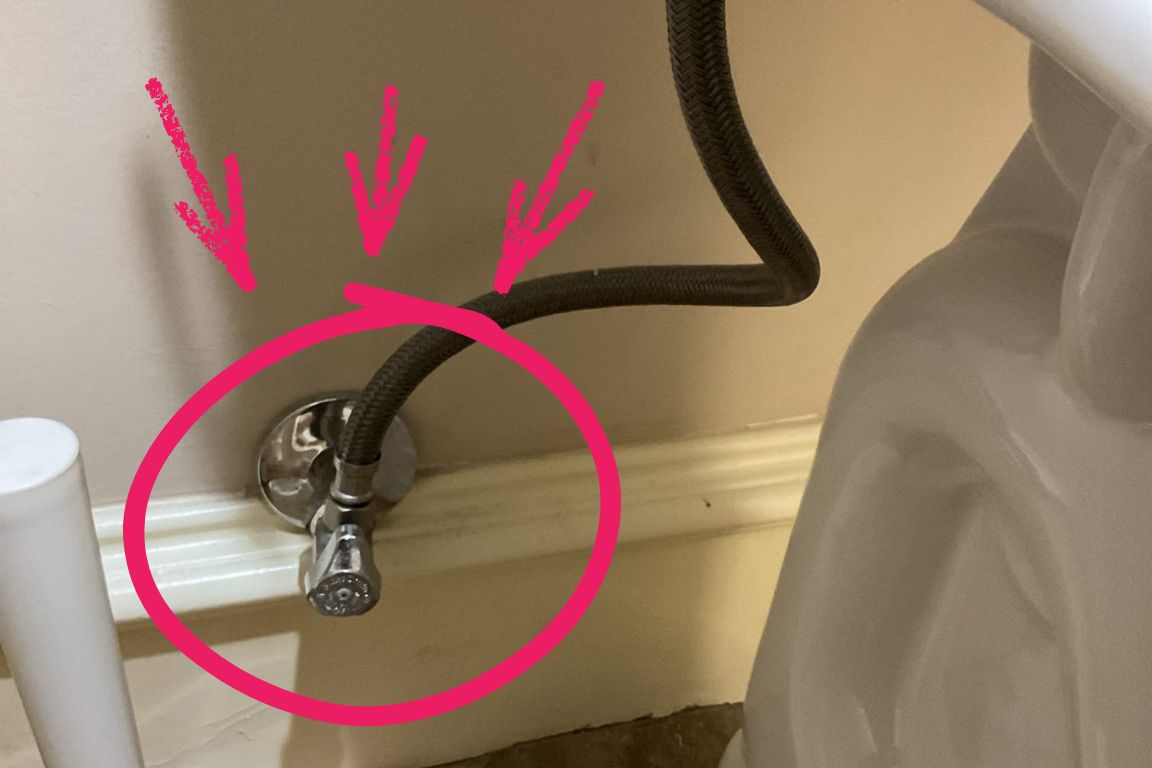 close up of toilet shut-off valve with circle and arrows to indicate its location, helpful during overflowing toilet crisis